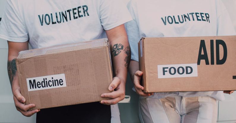 Fundraising - Man and Woman Carrying Medicine and Food Labelled Cardboard Boxes Behind a White Van